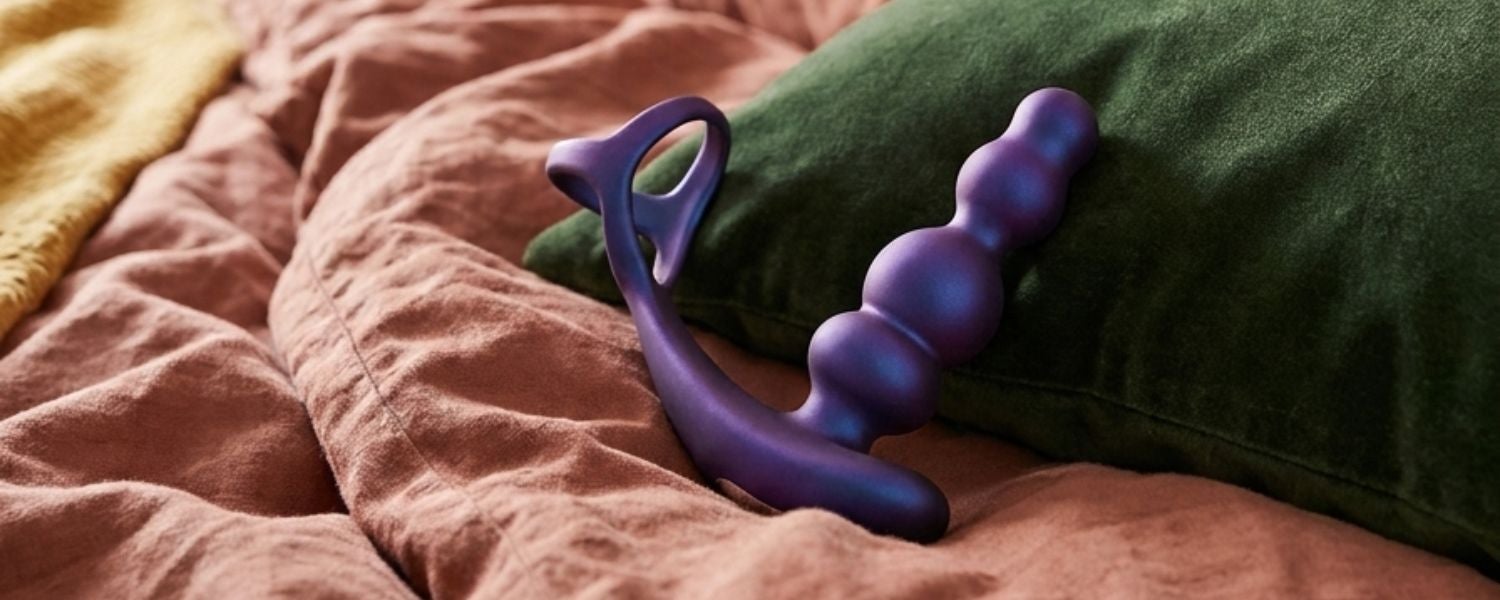Purple Hueman Stellar Force anal sextoy placed on a colourful bed with a pink blanket and green cushion.