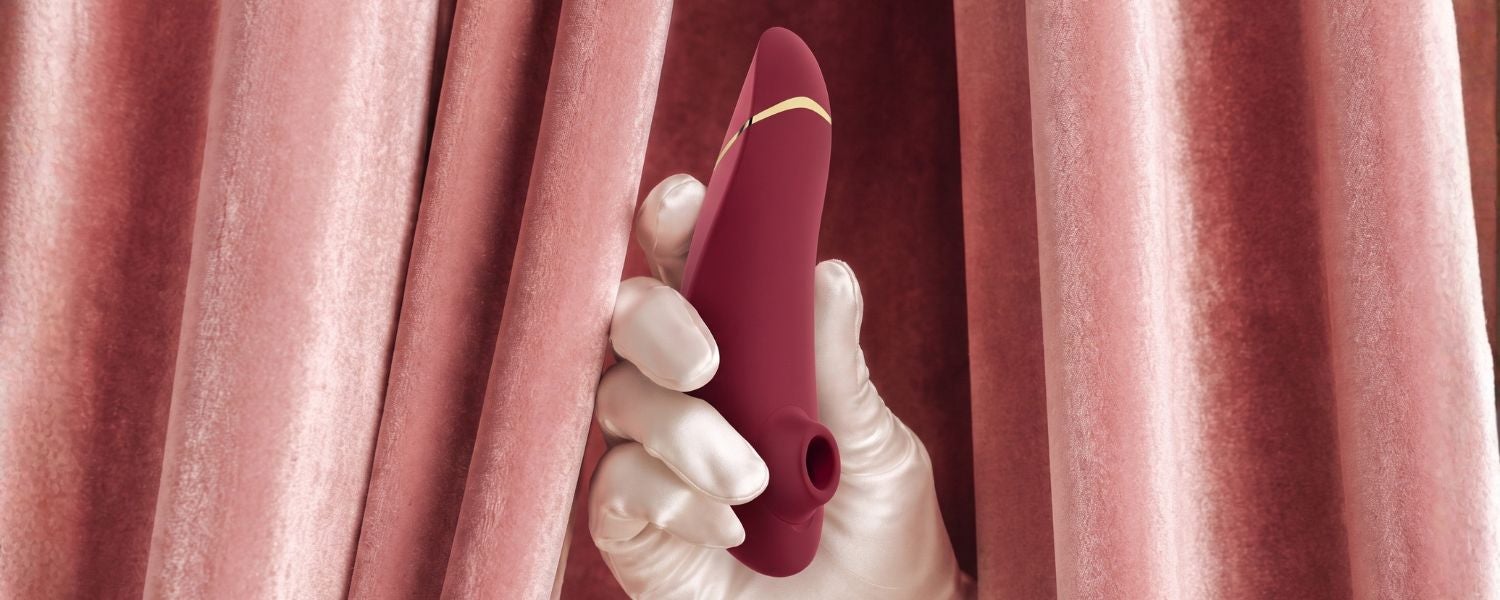 Le Womanizer Next dans la main, sur fond rose, pour le comparatif des Womanizer