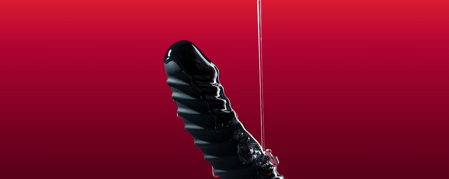 Schwarzer realistischer Dildo mit Gleitgel vor rotem Hintergrund.
