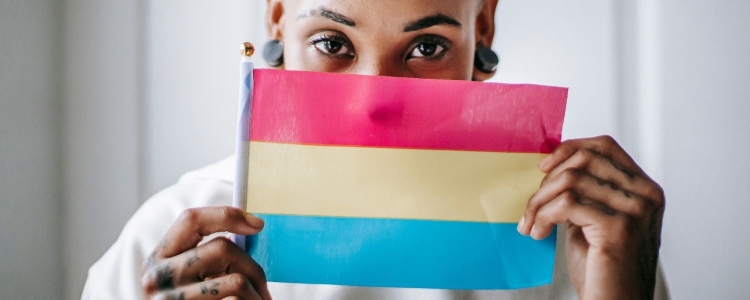 Person hält eine Pansexual-Pride-Flagge mit pinken, gelben und blauen Streifen vor sich.