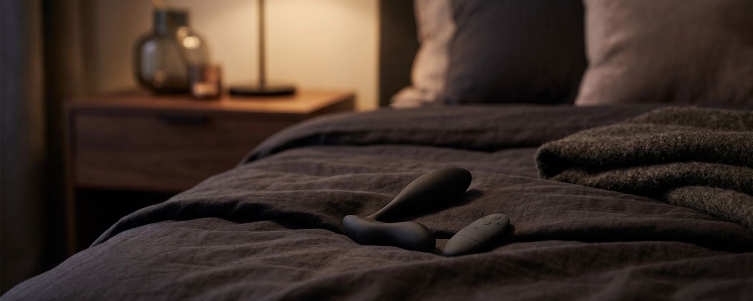 Stimulateur prostatique We-Vibe Vector+ posé sur un lit dans une ambiance sensuelle