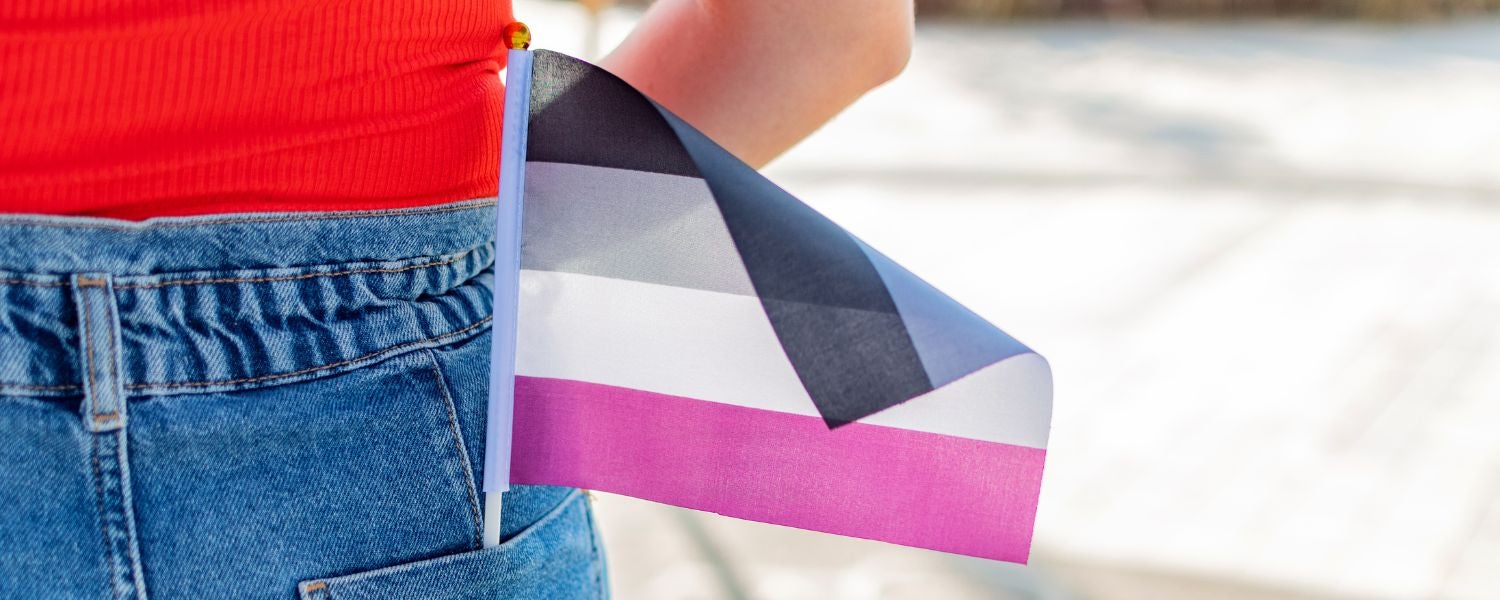 Gros plan sur une personne portant un drapeau de la fierté asexuelle dans la poche arrière de son jean. Le drapeau arbore les couleurs noir, gris, blanc et violet.