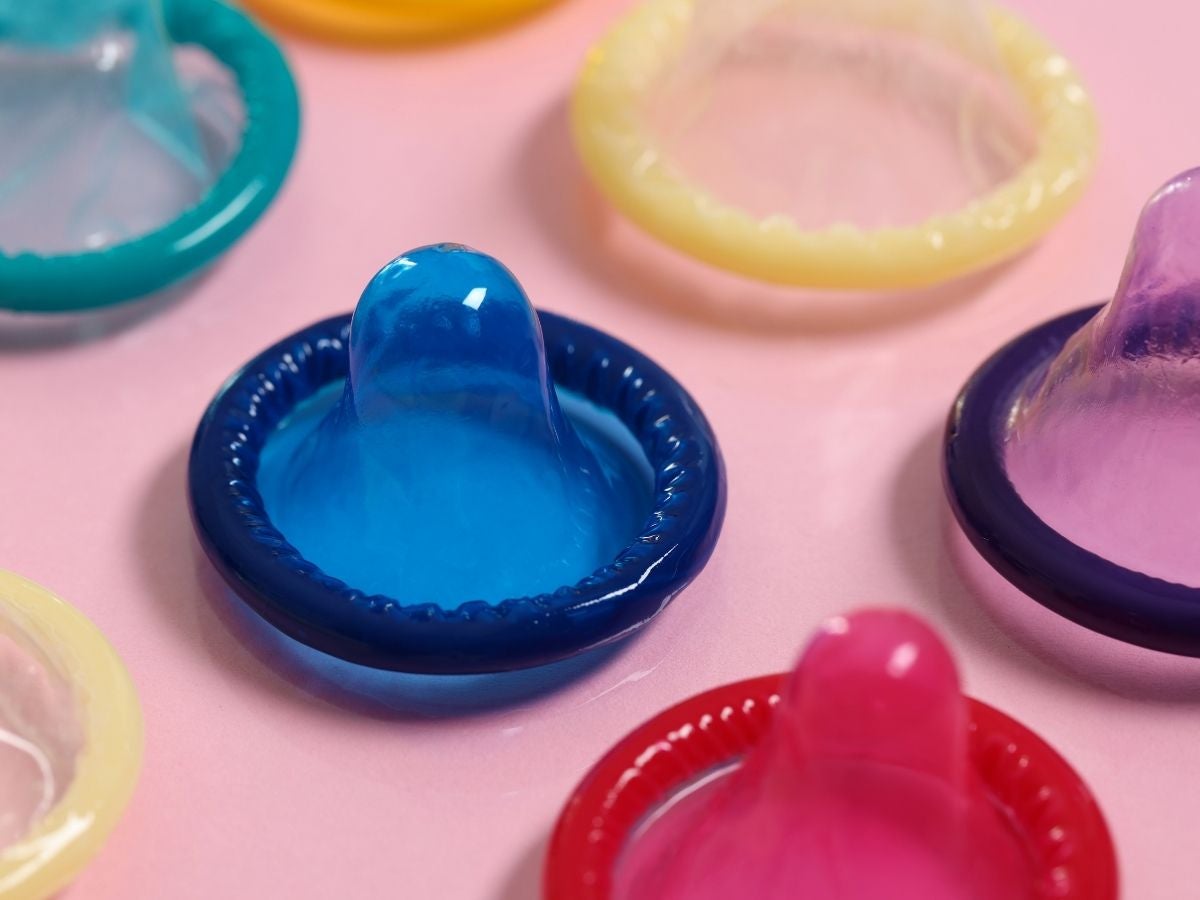 Mehrere bunte Kondome in verschiedenen Farben liegen auf einem rosafarbenen Hintergrund.