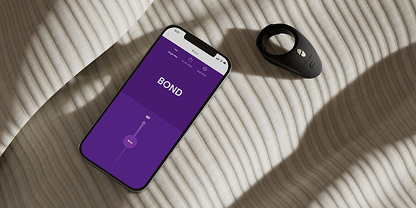 A We-Vibe Bond and a smartphone displaying the We-Vibe app, on neutral fabric.
