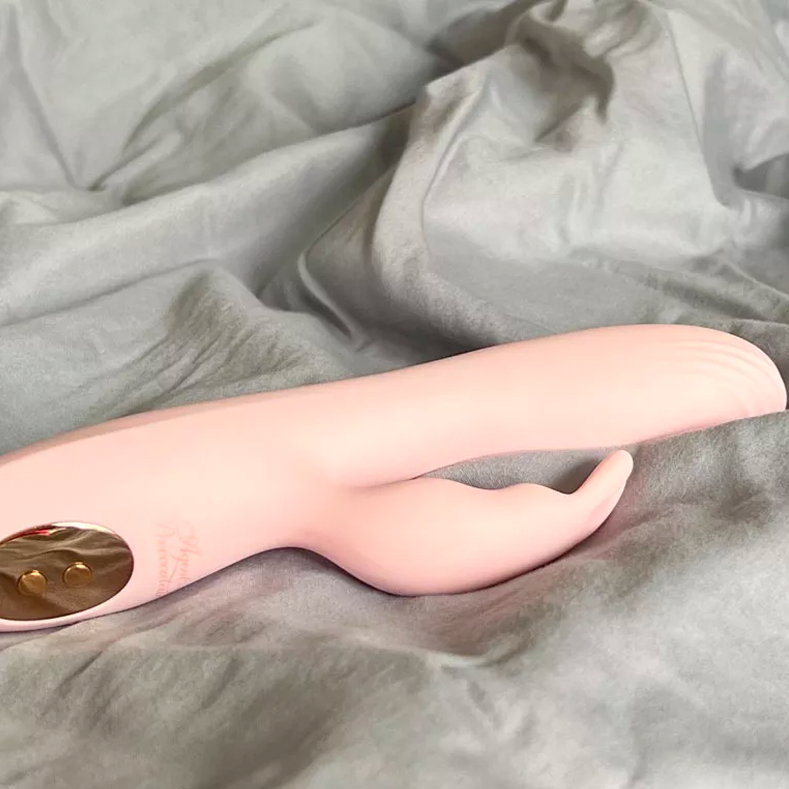 Ein rosafarbener Agent Provocateur x Lovehoney Bunny Hop Kaninchenvibrator auf grauem Bettzeug