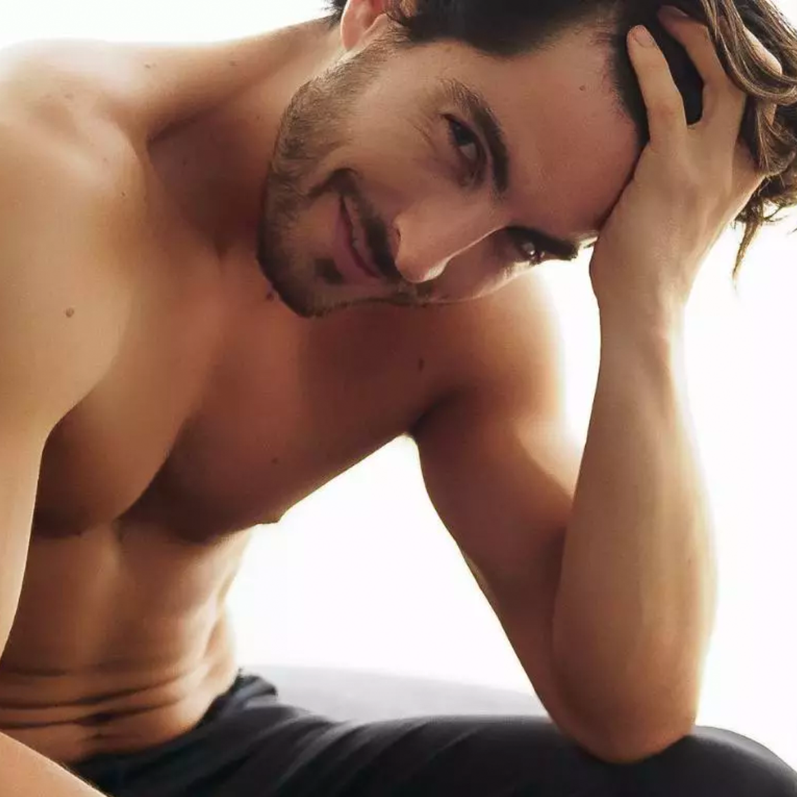 A shirtless man with his hand in his hair, smiling