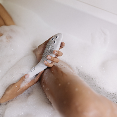 Eine Person, die einen Womanizer Wave in der Badewanne hält